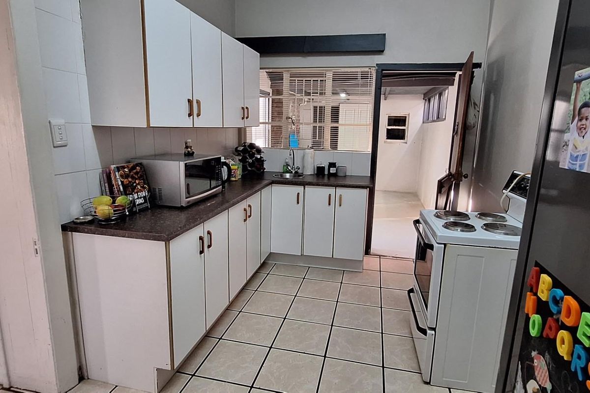A functional kitchen featuring white cabinetry, laminate countertops, tiled flooring, and a freestanding stove, with direct access to an adjacent utility area.