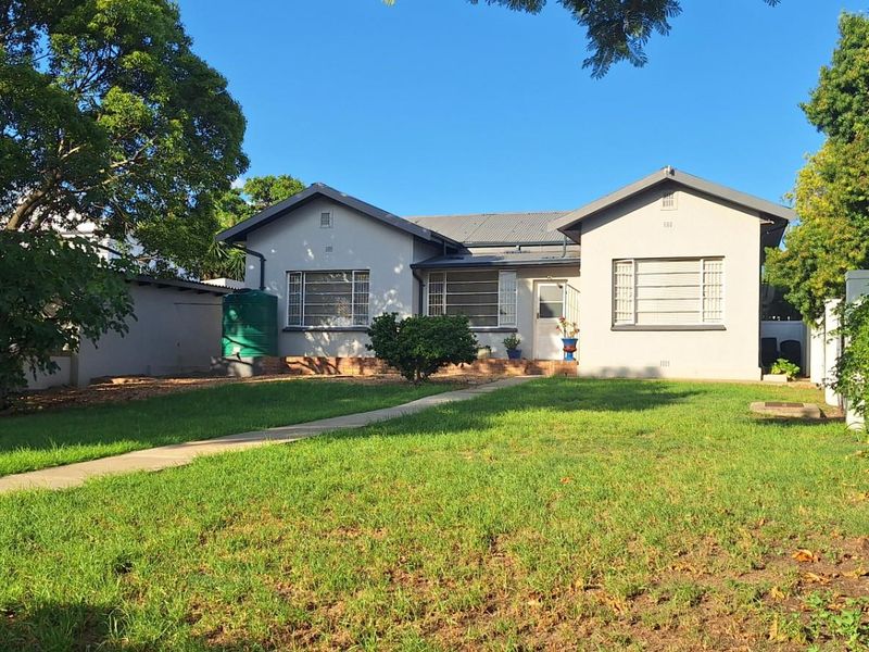 A well-maintained single-story residential house featuring a front garden, paved walkway, and a green water storage tank.