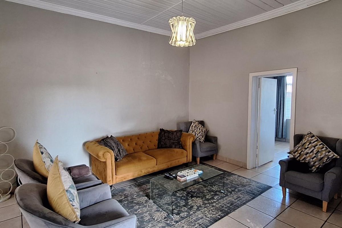 A spacious living room featuring neutral wall finishes, tiled flooring, and a classic ceiling design with a central light fixture.