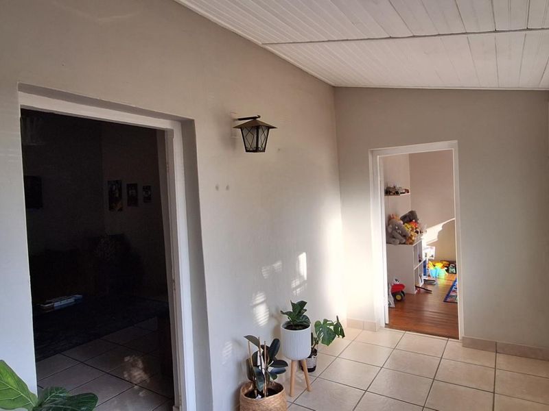 A bright, tiled hallway or sunroom area featuring neutral walls, a white timber-paneled ceiling, and access to adjacent living spaces.
