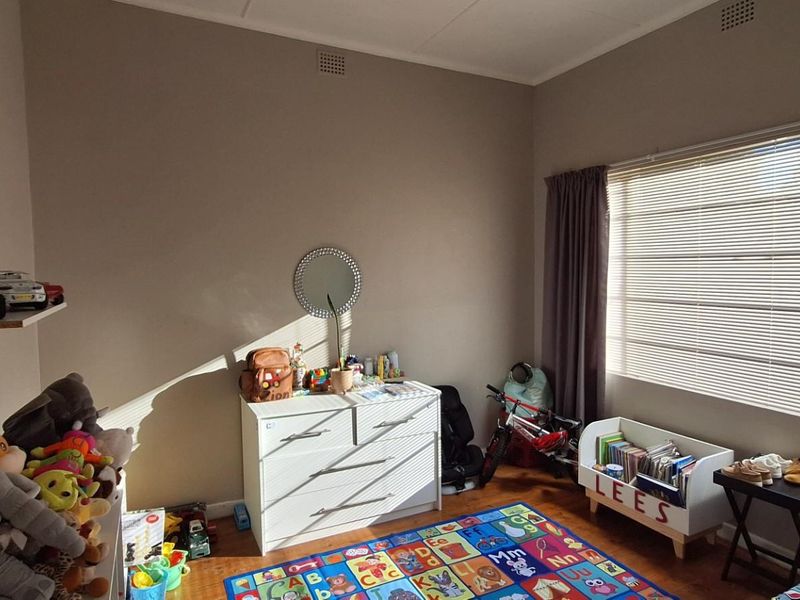A bedroom featuring timber flooring, large window with venetian blinds, and neutral wall finishes.