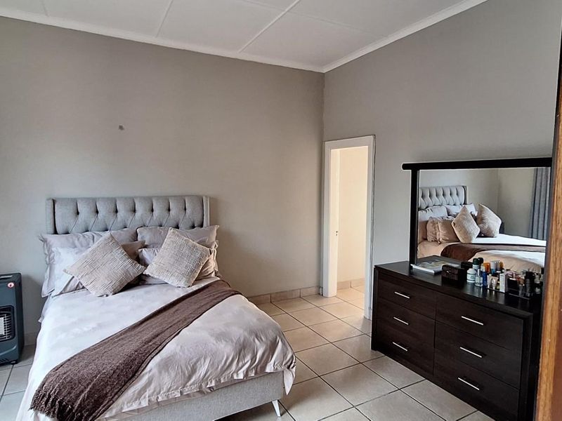 A well-lit bedroom featuring neutral wall tones, tiled flooring, and a doorway leading to an adjacent room.