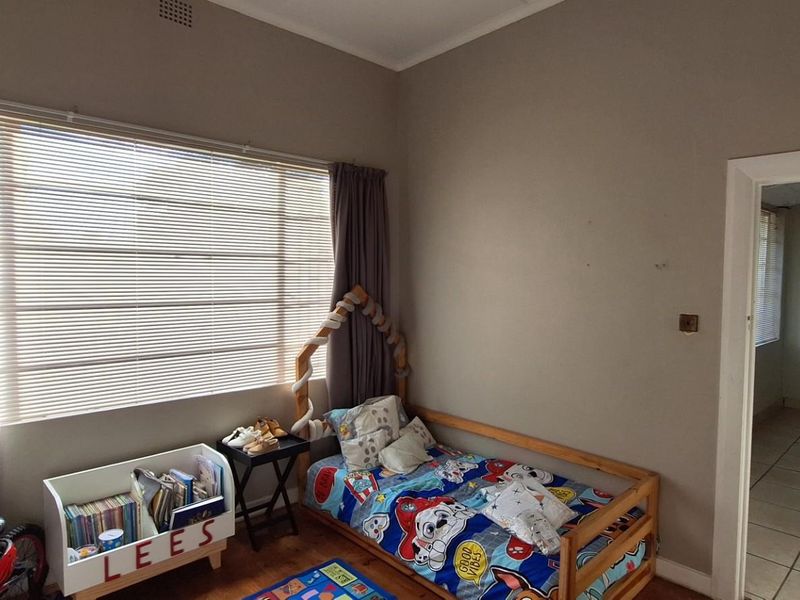 A bedroom featuring a large window with blinds, tiled flooring, and a doorway leading to an adjacent room.