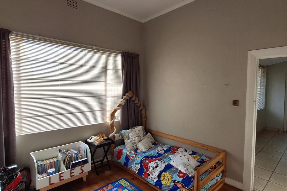 A bedroom featuring a large window with blinds, tiled flooring, and a doorway leading to an adjacent room.
