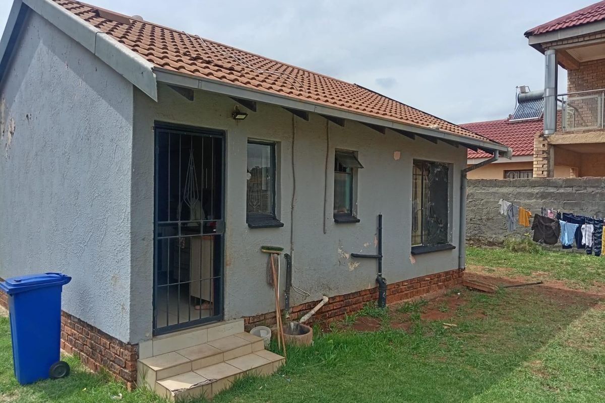 Rear view of a detached residential structure featuring a tiled roof, security gate, and exterior wall finishes requiring maintenance.