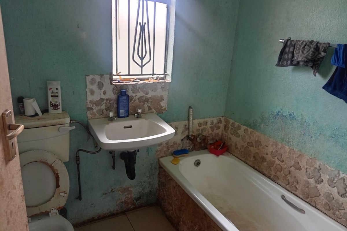 A dated bathroom featuring a standard bathtub, wall-mounted basin, and toilet, requiring significant renovation and repair to wall finishes and fixtures.