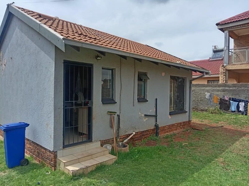 Rear view of a detached residential structure featuring a tiled roof, security gate, and exterior wall finishes requiring maintenance.