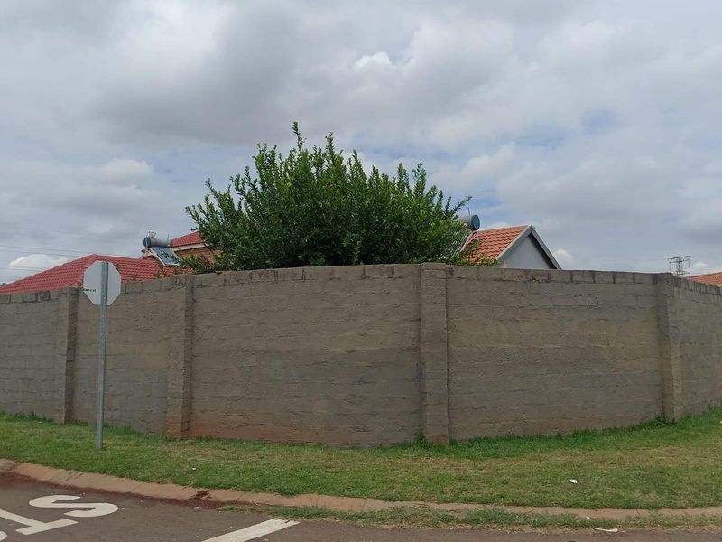 Street view of the property featuring a high, unfinished concrete perimeter wall and a tiled roof with solar water heating panels.