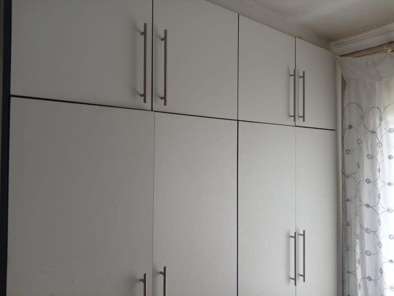 A bedroom featuring floor-to-ceiling built-in white cabinetry with modern stainless steel handles, providing ample integrated storage space.