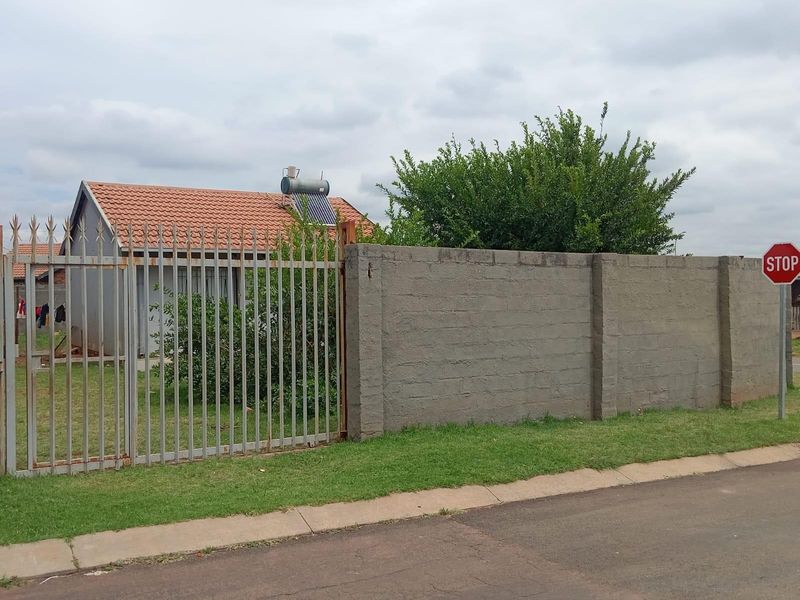 Front view of the property featuring a metal security gate, a concrete block boundary wall, and a roof-mounted solar geyser system.