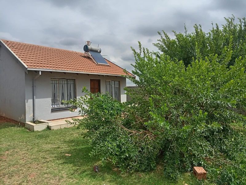 Rear view of a single-story house featuring a tiled roof, solar water heating system, and security bars on windows, set within a garden area.