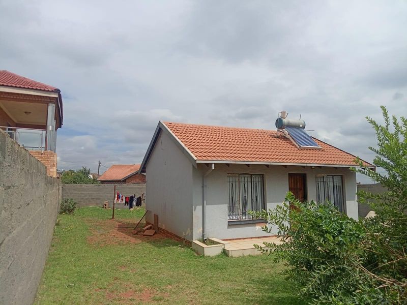 A detached single-story house featuring a tiled roof, solar water heating system, and security bars on windows, set within a private fenced yard.