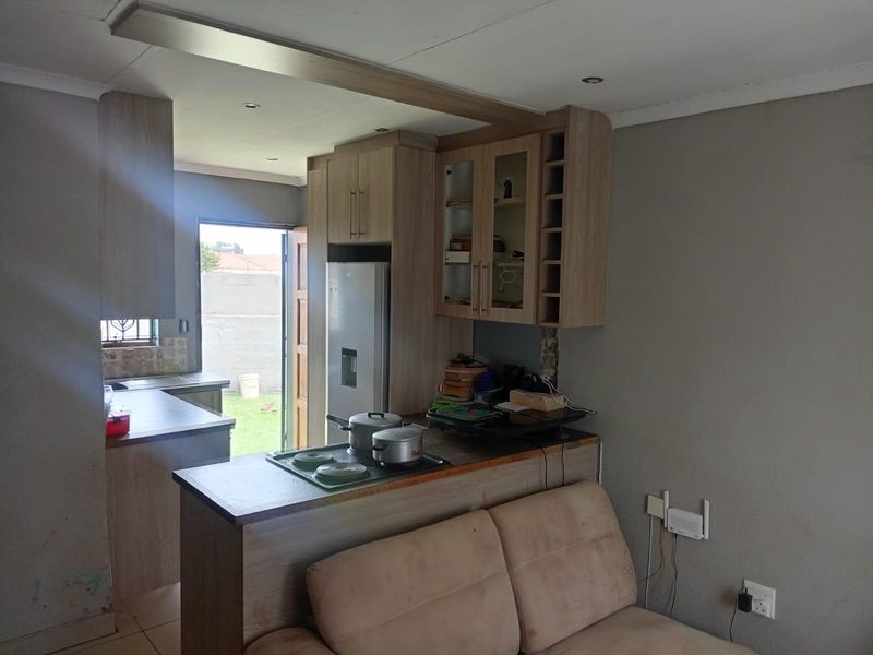Open plan kitchen featuring light wood cabinetry, integrated hob, and breakfast counter, seamlessly connecting to the living area with direct outdoor access.