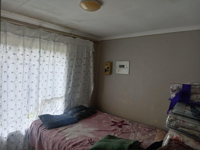 A bedroom featuring a window with curtains, a wall-mounted alarm keypad, and a central ceiling light fixture.