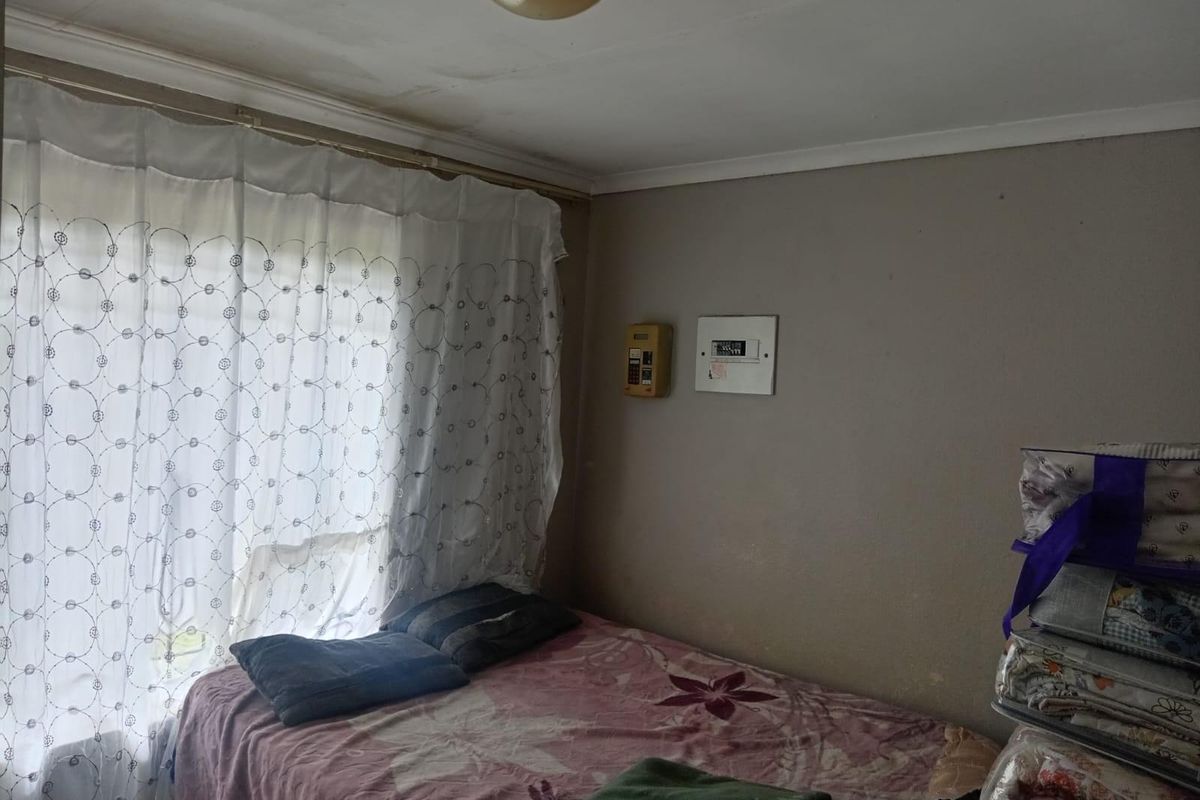 A bedroom featuring a window with curtains, a wall-mounted alarm keypad, and a central ceiling light fixture.