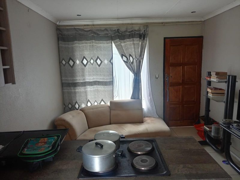 Open plan living area featuring a built-in kitchen counter with a solid plate hob, tiled flooring, and direct access to an exterior door.