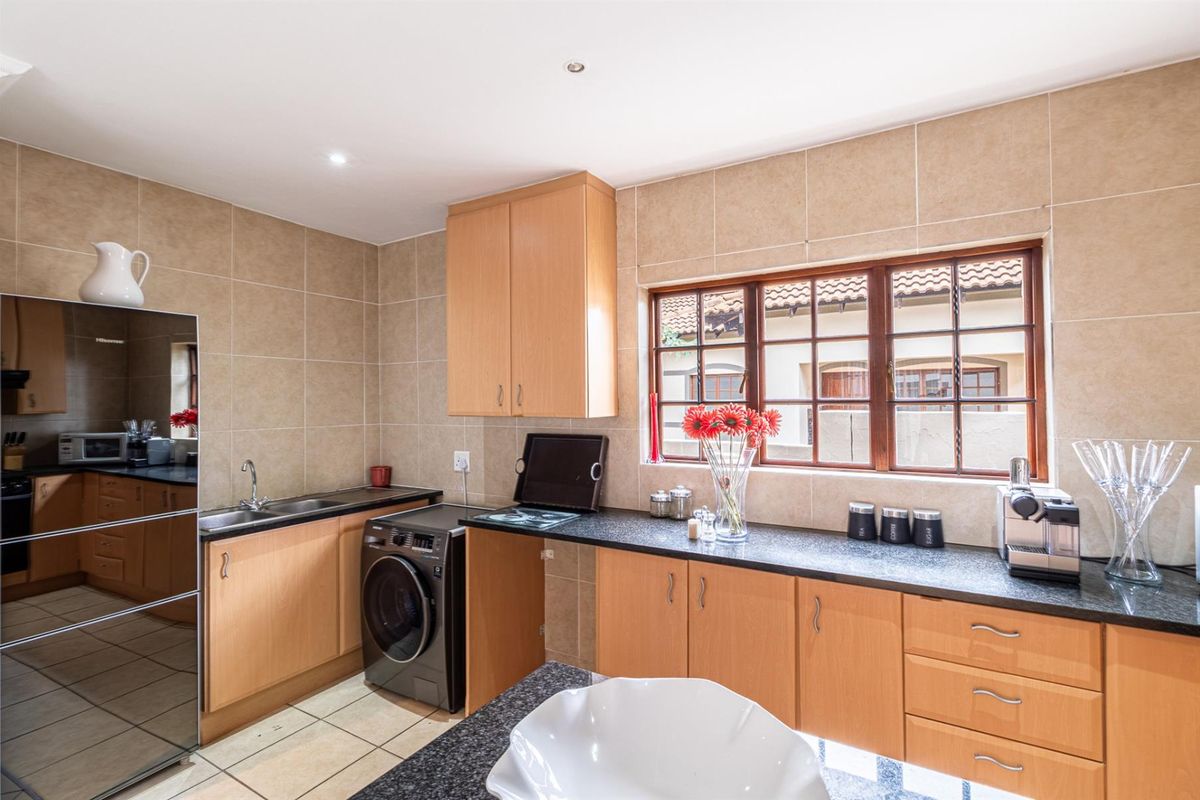A functional kitchen featuring light wood cabinetry, dark granite countertops, tiled splashbacks, and integrated space for laundry appliances.