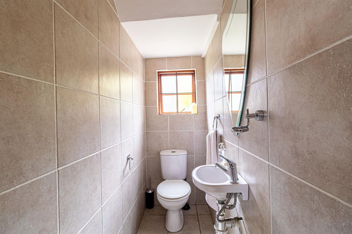 A compact guest bathroom featuring floor-to-ceiling neutral wall tiles, a wall-mounted basin, and a standard toilet.
