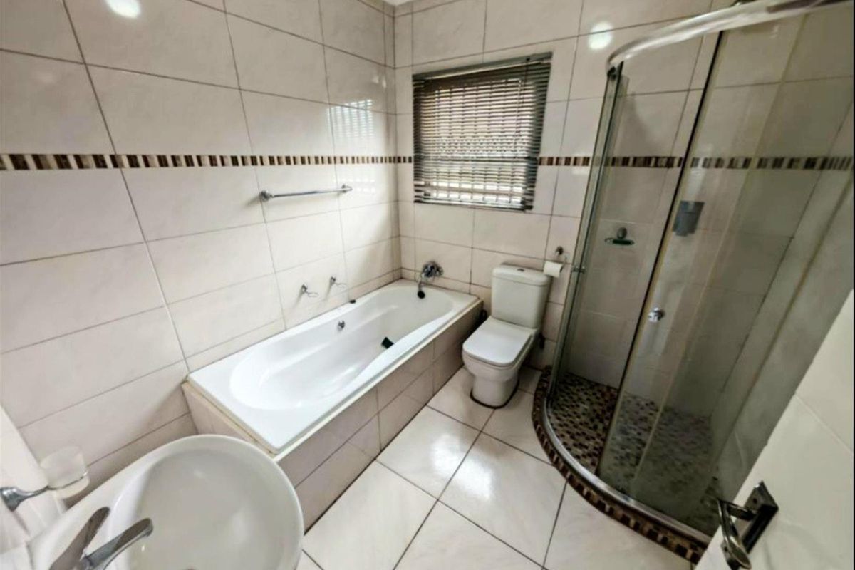 A well-maintained bathroom featuring a built-in bathtub, a separate glass-enclosed shower, a toilet, and a pedestal sink with tiled walls and flooring.