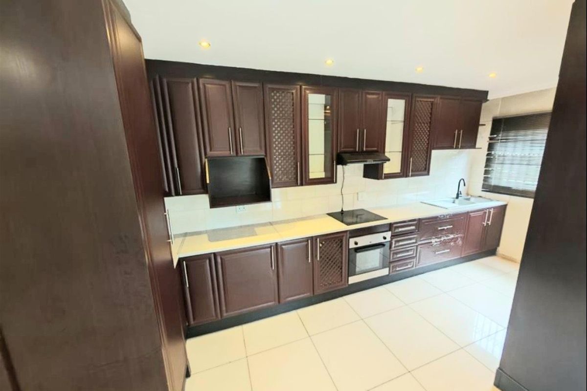 A functional kitchen featuring dark wood cabinetry, integrated oven, electric hob, extractor fan, and tiled flooring with a neutral backsplash.