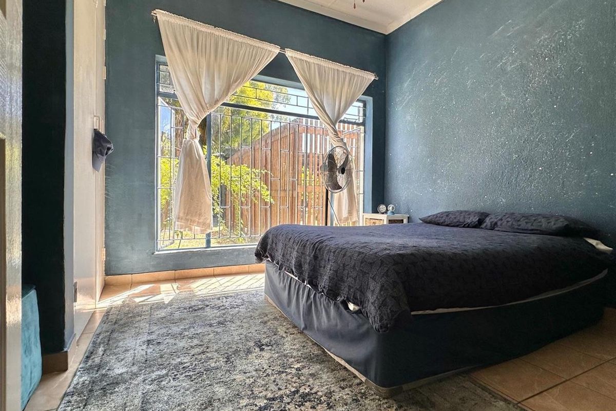 A bedroom featuring tiled flooring, a large window with security bars, and dark blue painted walls.