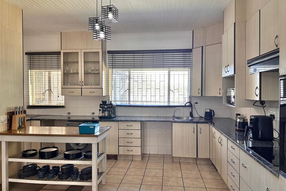 Spacious kitchen featuring light wood-tone cabinetry, dark granite countertops, tiled flooring, and a central island with open shelving.