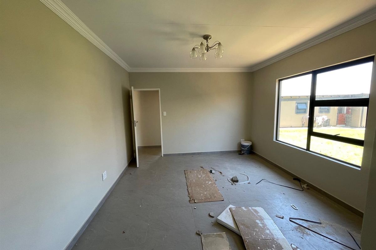 An empty bedroom featuring tiled flooring, ceiling cornice, and large aluminium-framed windows, currently undergoing final finishing touches.