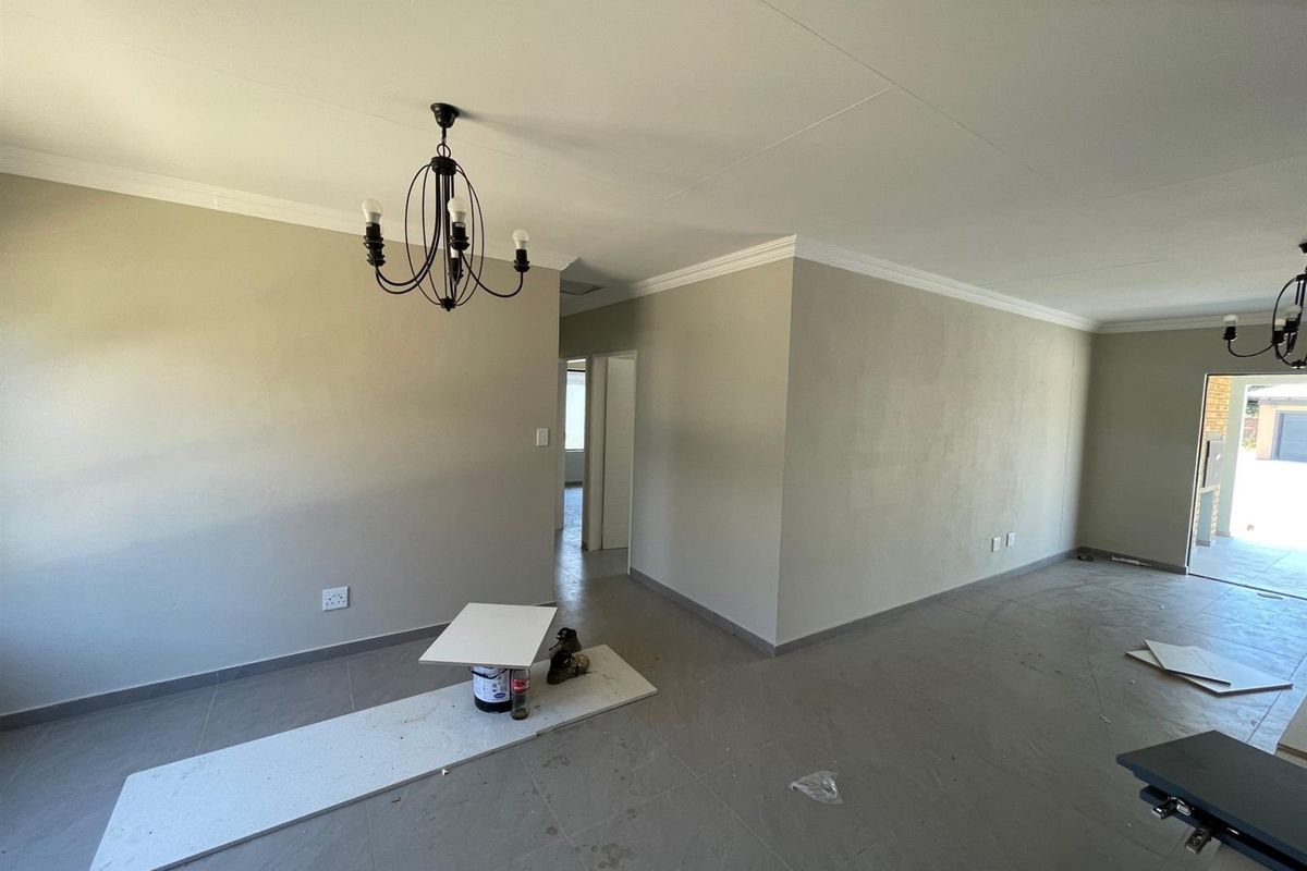 An open-plan living area featuring neutral wall tones, tiled flooring, and decorative ceiling cornices, currently in a vacant state awaiting final finishes.