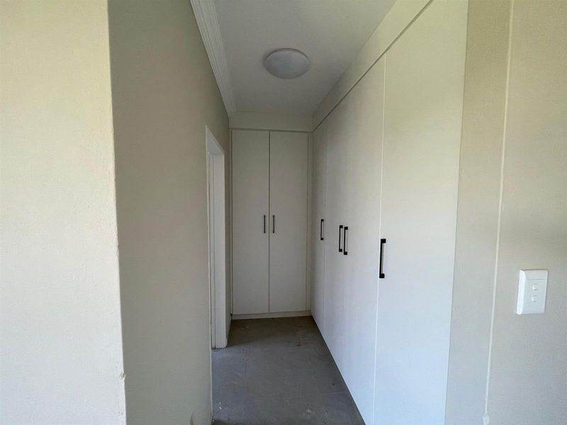 A functional hallway featuring extensive built-in storage cupboards with modern hardware and neutral wall finishes, currently awaiting final flooring installation.