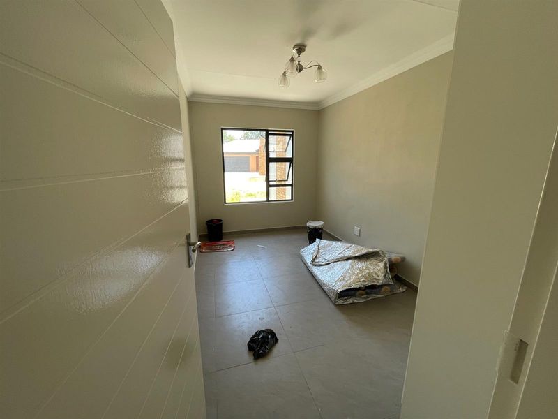 A clean, empty bedroom featuring neutral tiled flooring, modern aluminium window frames, and simple ceiling finishes, ready for personalization.