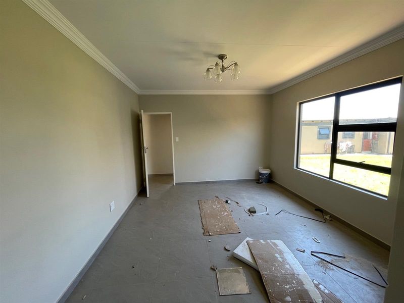 An empty bedroom featuring tiled flooring, ceiling cornice, and large aluminium-framed windows, currently undergoing final finishing touches.