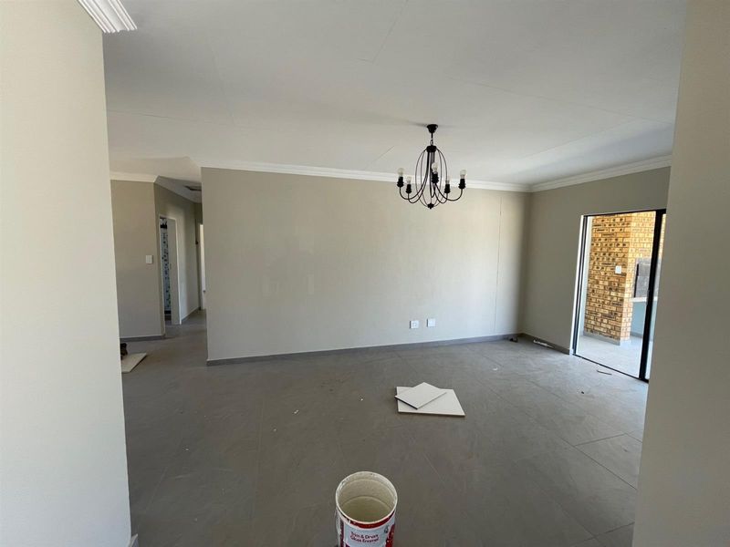 Spacious, empty living area featuring neutral tiled flooring, cove cornicing, and a modern chandelier, with direct access to an outdoor patio area.