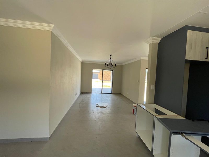 An open-plan living and kitchen area featuring neutral walls, crown molding, tiled flooring, and a sliding door leading to the exterior.
