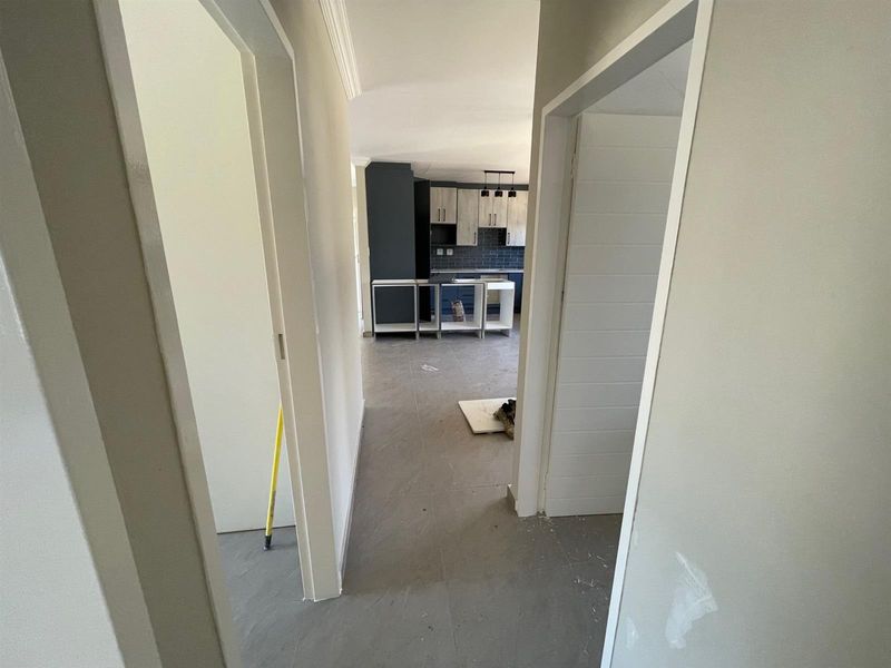 A view from a hallway looking into an unfinished kitchen area featuring modern cabinetry and a tiled backsplash, currently undergoing renovation.