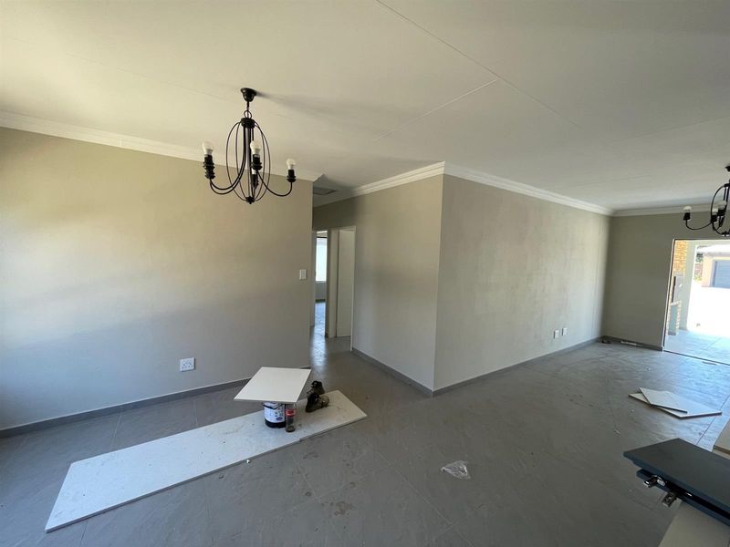 An open-plan living area featuring neutral wall tones, tiled flooring, and decorative ceiling cornices, currently in a vacant state awaiting final finishes.