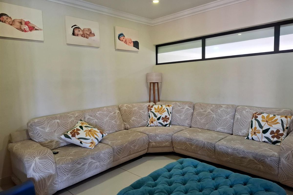 A comfortable living room featuring neutral tiled flooring, recessed downlighting, and a high-level horizontal window providing natural light.