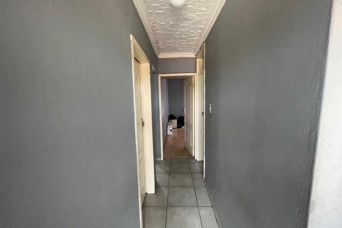 A functional hallway featuring grey painted walls, tiled flooring, and a textured ceiling with traditional cornicing, connecting multiple rooms within the apartment.