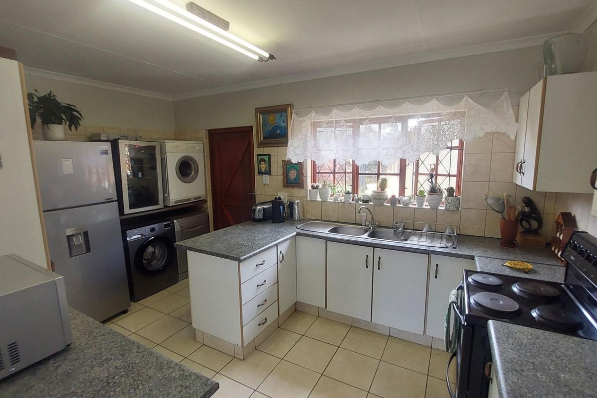 Functional kitchen featuring L-shaped laminate countertops, double basin sink, tiled backsplash, and integrated space for laundry appliances.