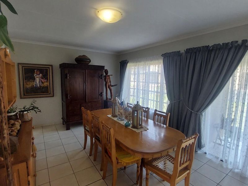 A dining room featuring tiled flooring and large windows with curtains, providing natural light and access to the outdoor area.