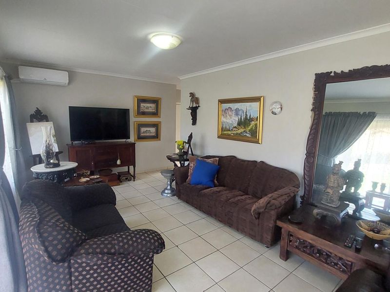 A spacious living room featuring neutral tiled flooring, coved ceilings, and a wall-mounted air conditioning unit.