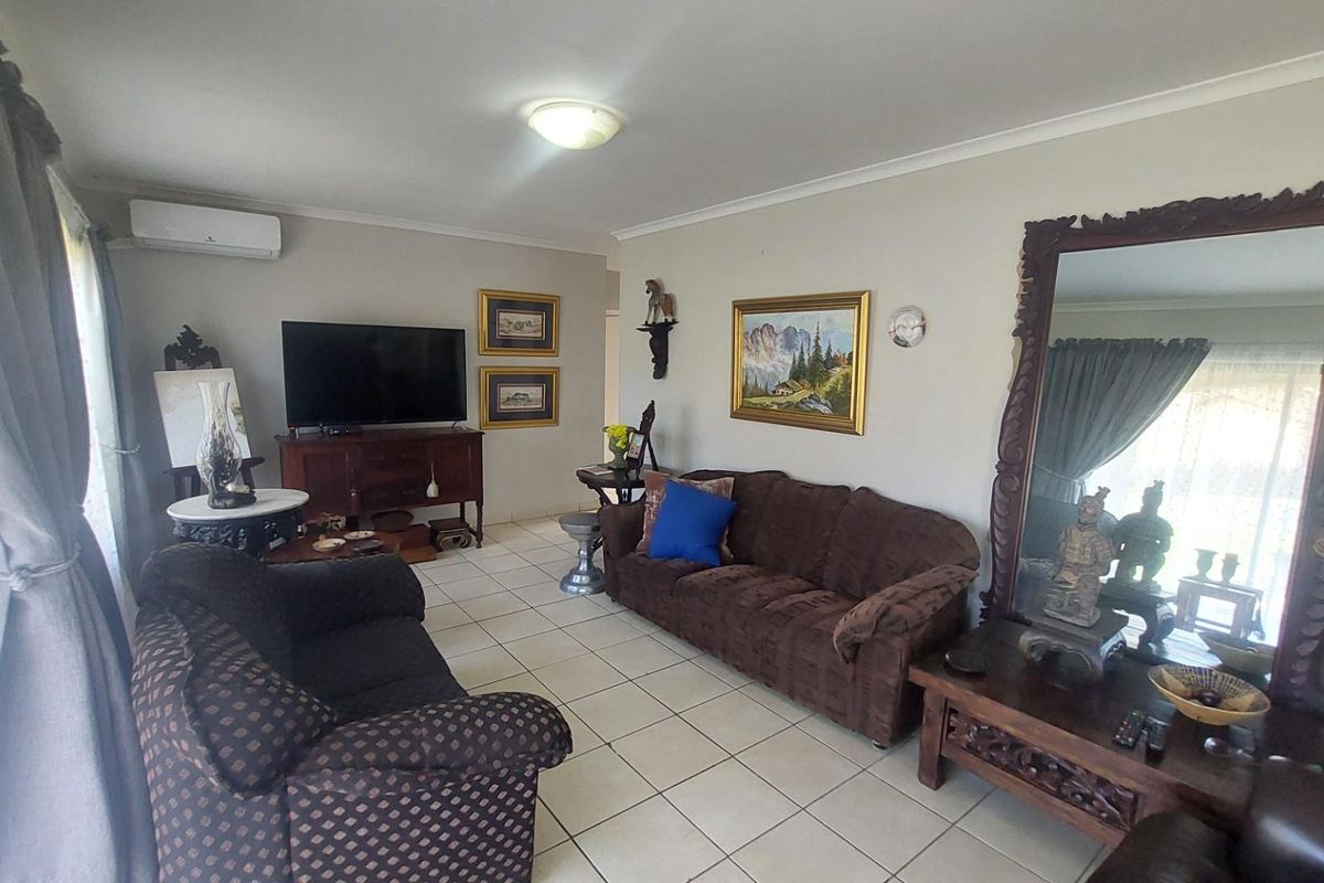 A spacious living room featuring neutral tiled flooring, coved ceilings, and a wall-mounted air conditioning unit.