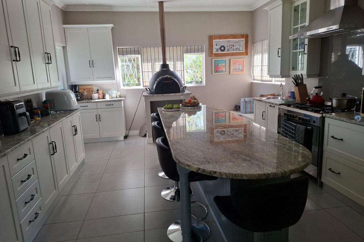 Spacious kitchen featuring granite countertops, a central island with breakfast bar, built-in oven with extractor fan, and a unique indoor pizza oven.