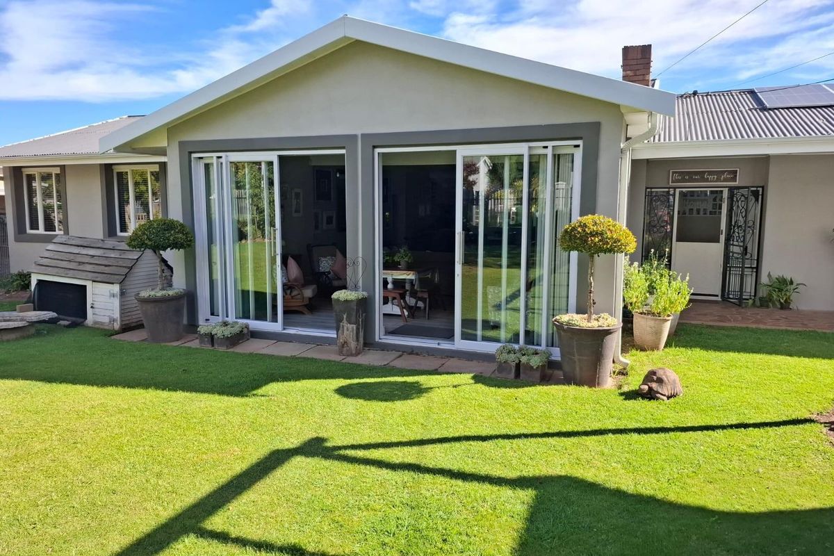 Rear view of the house featuring a well-maintained lawn, paved patio area, and large sliding glass doors providing seamless indoor-outdoor flow.