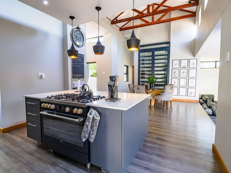 Modern open-plan kitchen and dining area featuring a central island with gas cooktop, exposed timber roof trusses, and integrated wine storage.