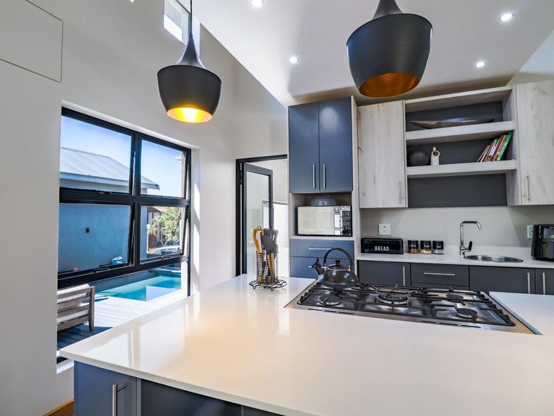 Modern kitchen featuring sleek two-tone cabinetry, stone countertops, a built-in gas hob, and large windows overlooking the pool area.