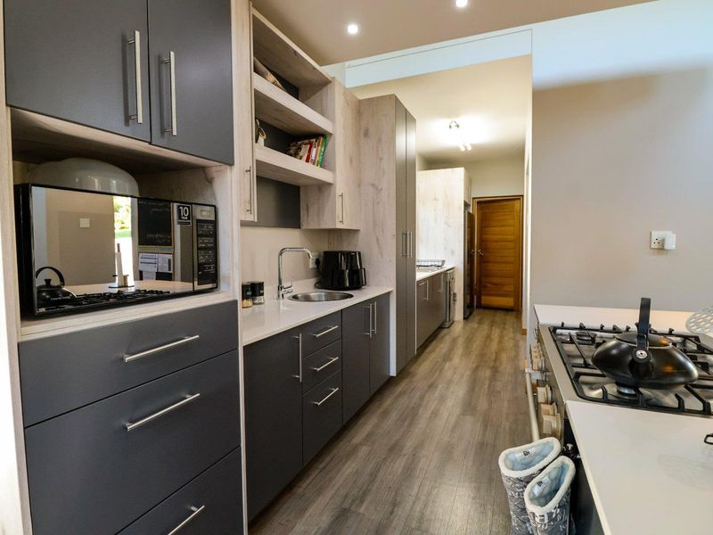 Modern kitchen featuring dark grey and light wood cabinetry, quartz countertops, gas hob, and durable laminate flooring with a clean, contemporary finish.