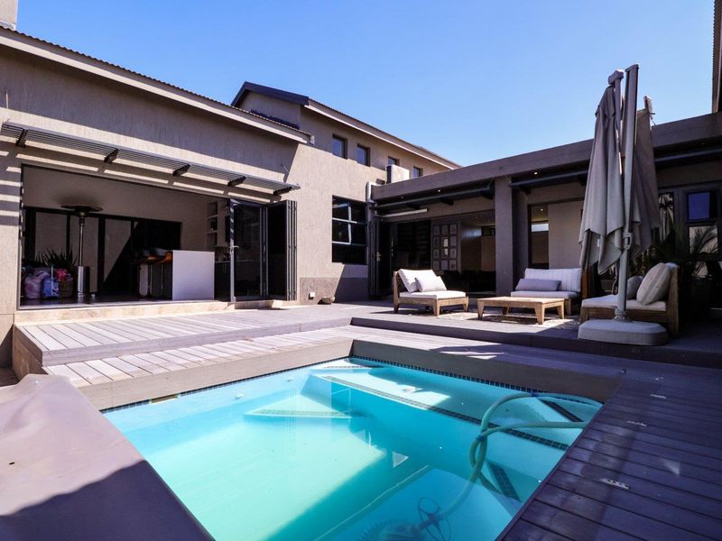 Outdoor entertainment area featuring a swimming pool with timber decking, covered patio space, and seamless indoor-outdoor flow through stacking doors.