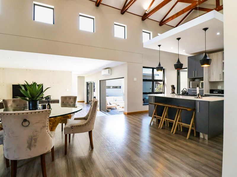 Spacious open-plan living and kitchen area featuring high vaulted ceilings with exposed timber beams, modern cabinetry, and seamless flow to the outdoor patio.