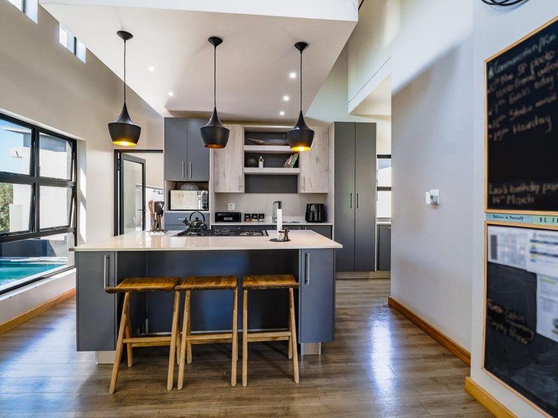 Modern kitchen featuring a central island with gas hob, sleek grey cabinetry, stone countertops, and stylish pendant lighting, creating a functional and contemporary cooking space.