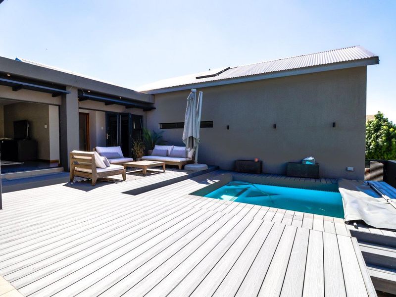 Outdoor entertainment area featuring a swimming pool and modern timber decking, seamlessly connected to the interior living space via large sliding glass doors.